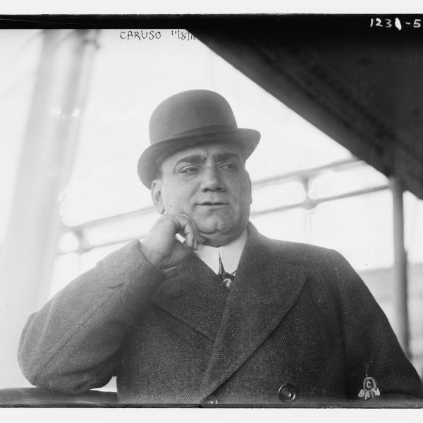 Man in bowler hat pondering with hand on cheek.