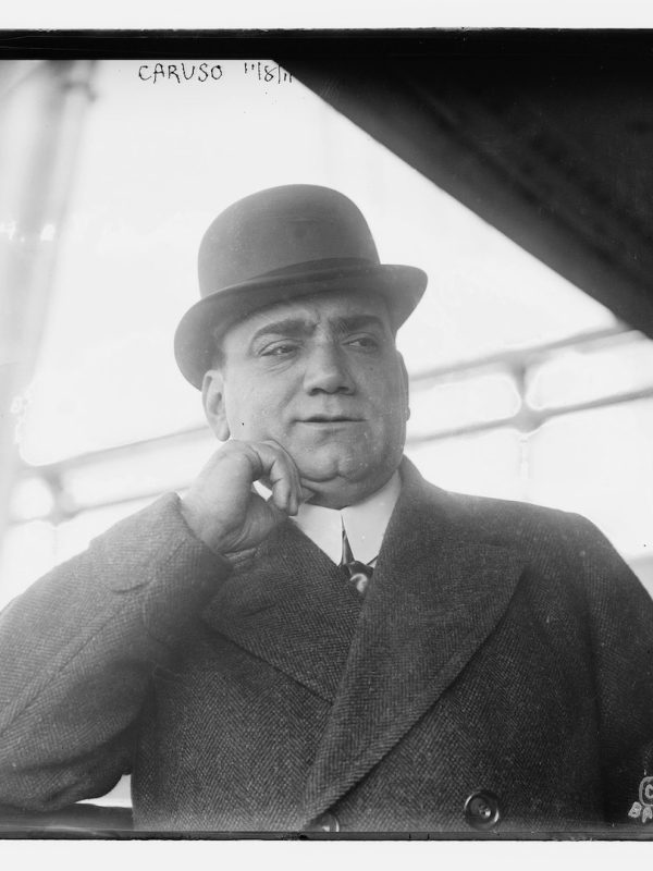 Man in bowler hat pondering with hand on cheek.