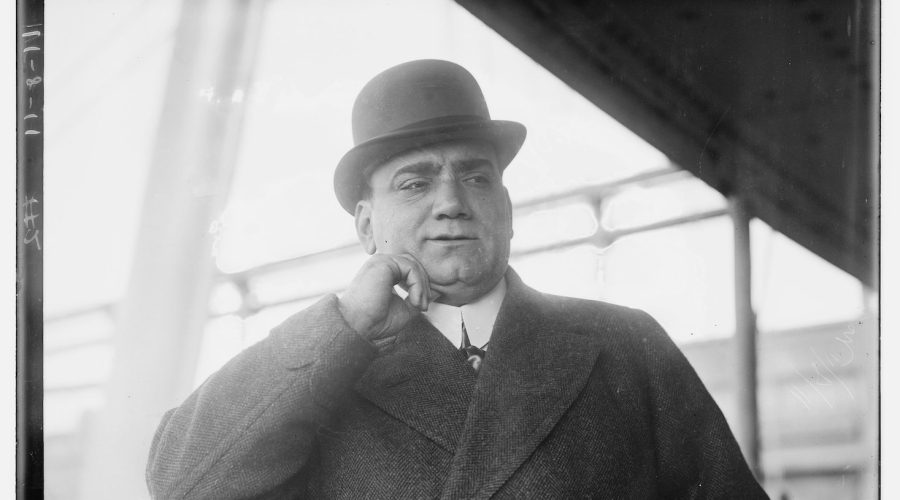 Man in bowler hat pondering with hand on cheek.