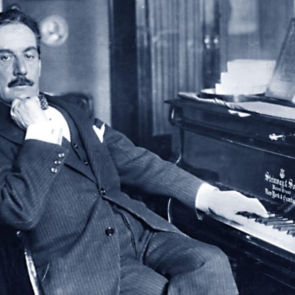 Gentleman in a suit sitting at a piano, resting his cheek on his hand.