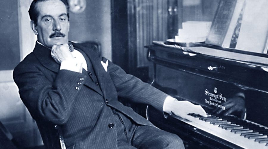 Gentleman in a suit sitting at a piano, resting his cheek on his hand.