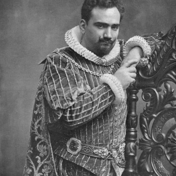 A man in elaborate Renaissance-style attire poses with one arm resting on an ornate piece of furniture.